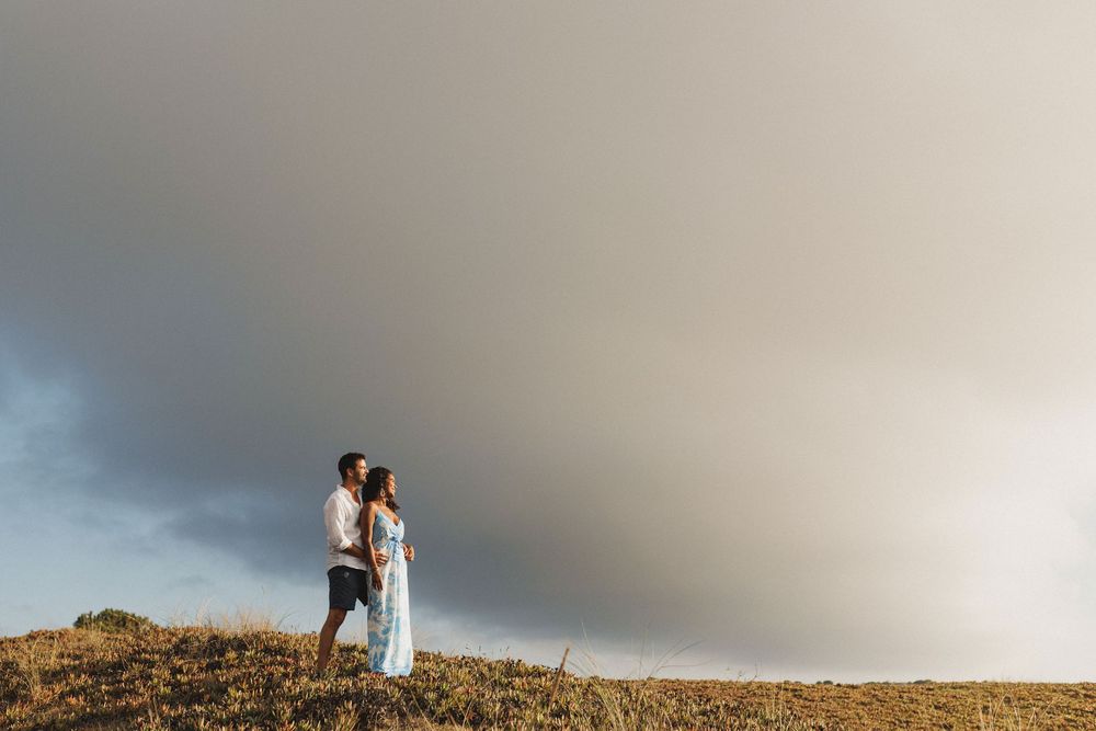 Pre wedding photoshoot in Sesimbra at Praia das Bicas with couple standing on cliff under dramatic sky