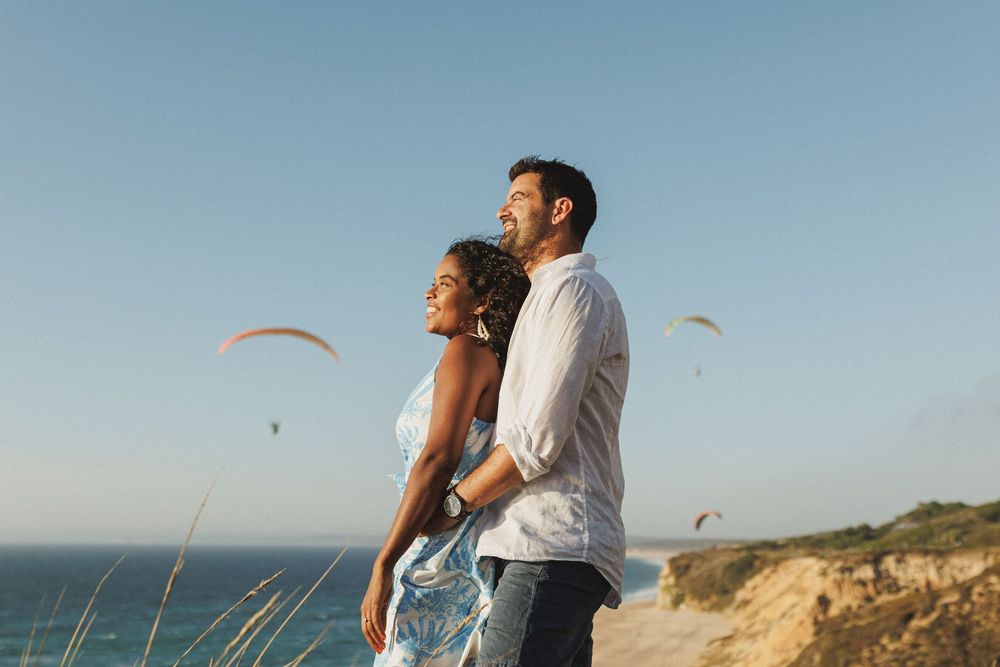 Couple enjoying scenic coastal view with paragliders during engagement session at Praia das Bicas Sesimbra
