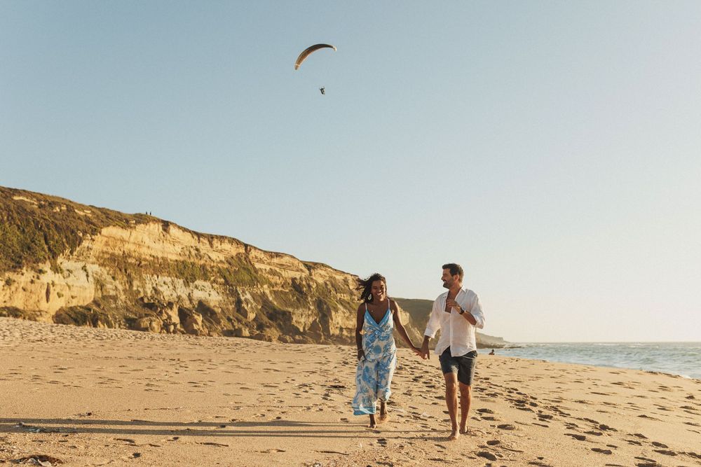 Couple walking hand in hand on Praia das Bicas beach during golden hour engagement session in Portugal