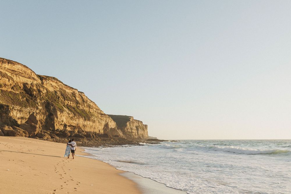 Couple walking along coastline with cliffs at Praia das Bicas during engagement photoshoot Portugal