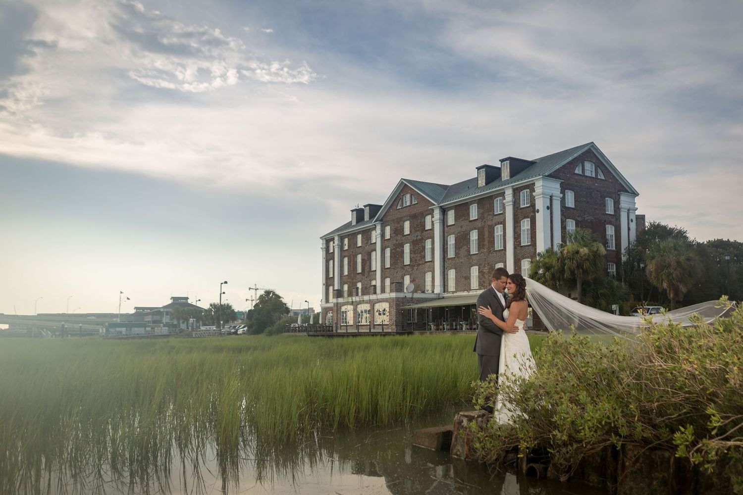 Panoramic view of a waterfront wedding ceremony with guests seated on white chairs by a scenic lake.