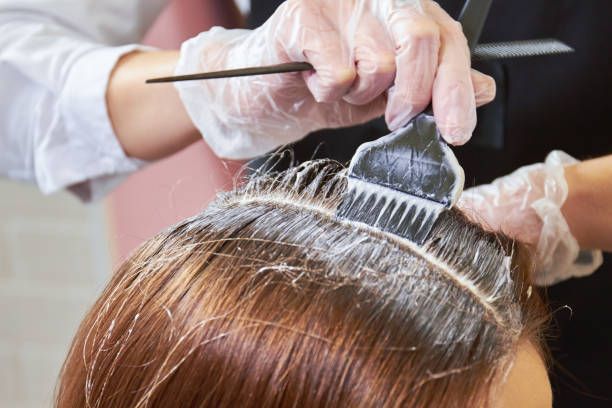 Hair stylist applying hair dye with brush to client's hair in salon.