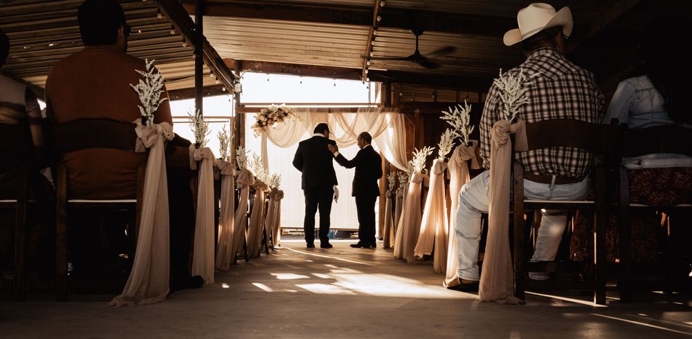 Silhouettes of wedding guests dancing and celebrating in a rustic barn venue with warm lighting and hanging decor.