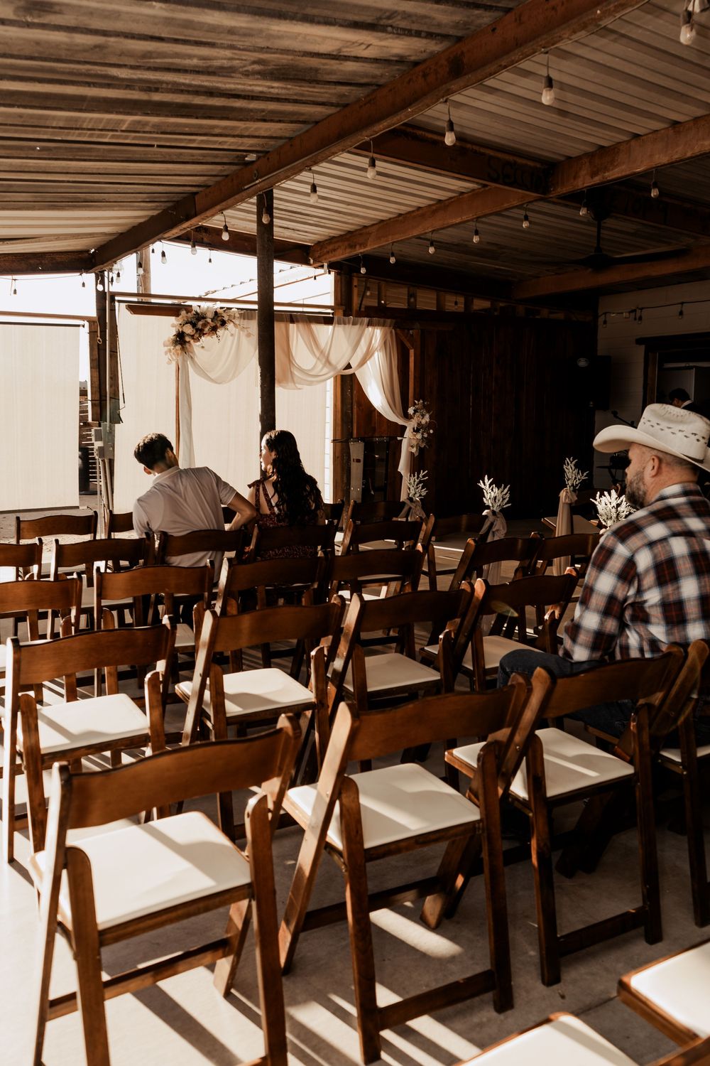 Rustic wooden folding chairs lined up in rows under a covered outdoor venue for a wedding ceremony.