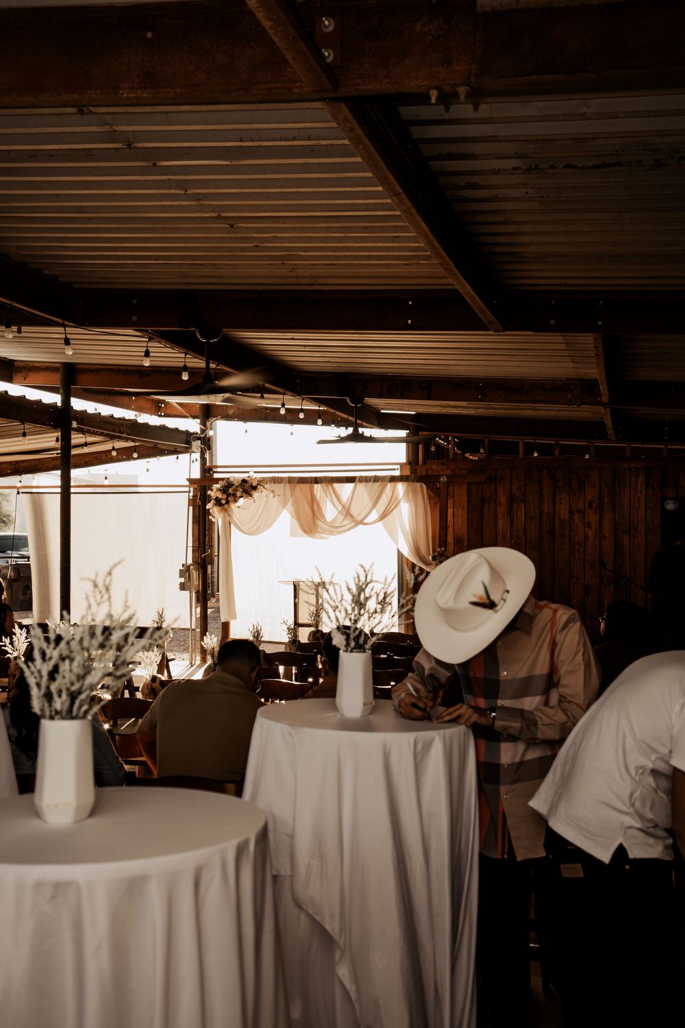 Wedding reception venue with white tablecloths and wooden ceiling beams creates an elegant rustic atmosphere.