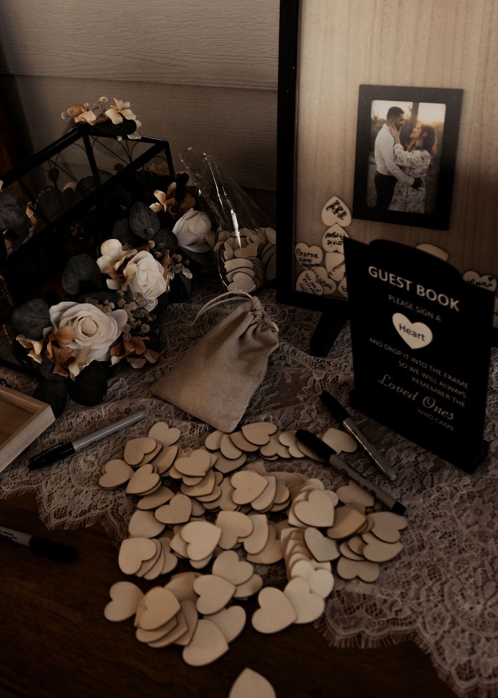 Wedding guest book with scattered wooden hearts and decorative elements on lace tablecloth in moody lighting.