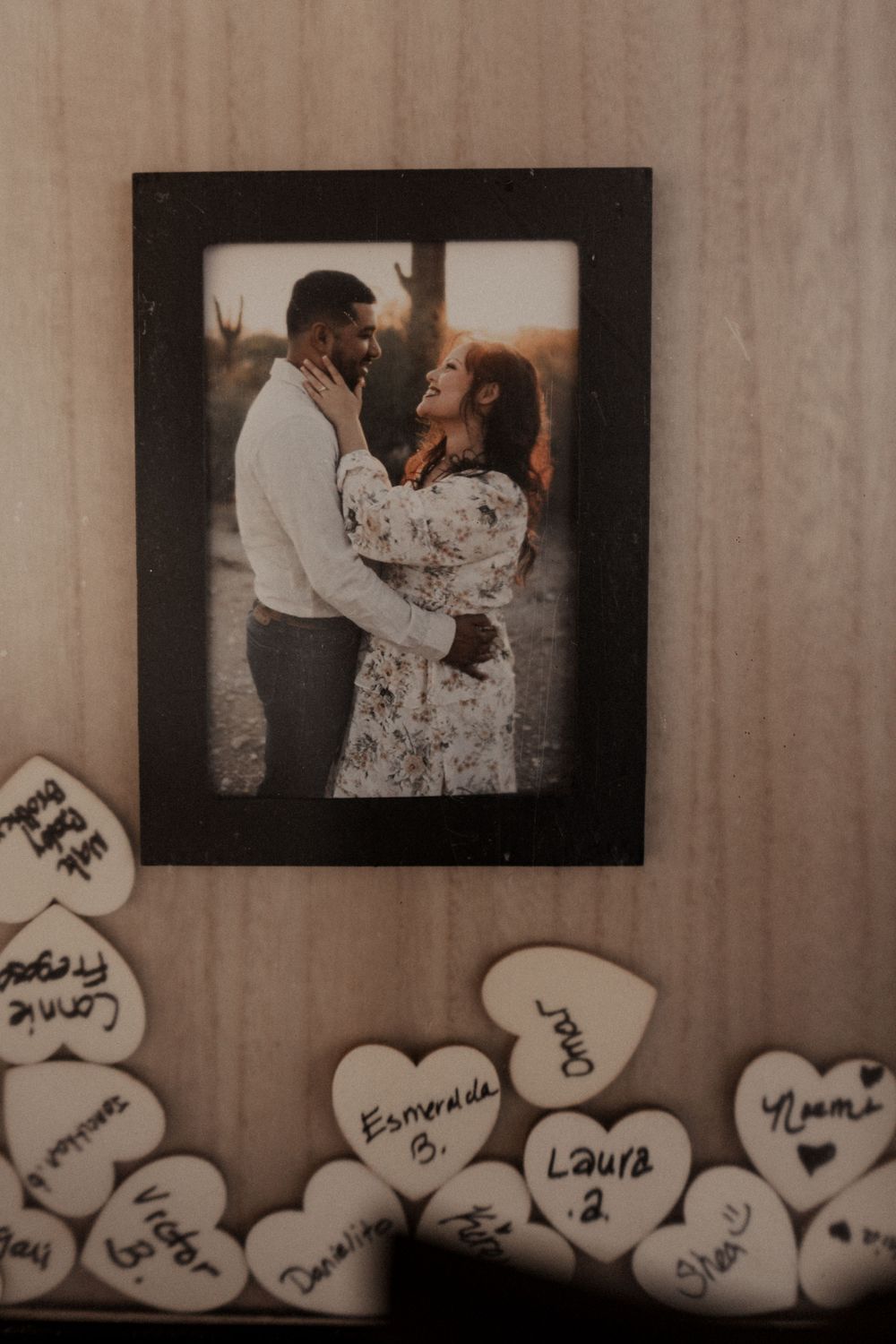 Wedding reception decor features black and white photos displayed above heart-shaped name cards on a wall.