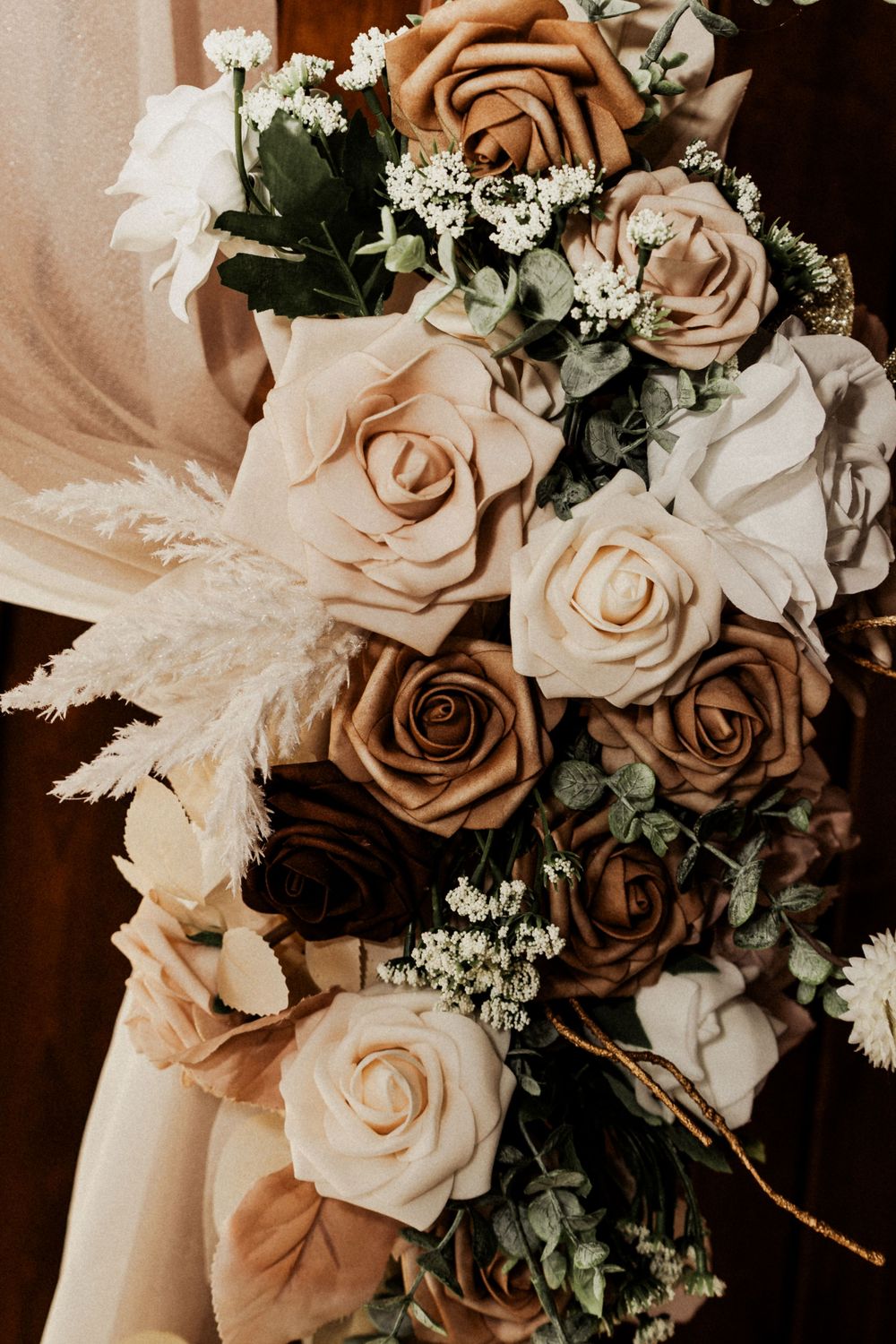 A romantic bouquet of brown and cream roses with baby's breath and pampas grass in a vintage-inspired arrangement.