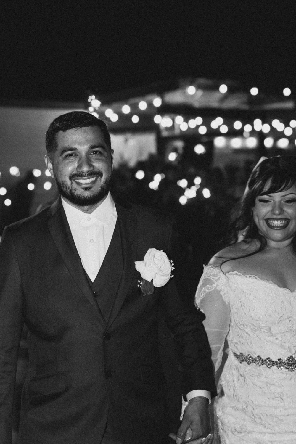 A happy couple shares joyful moments during their wedding reception with twinkling lights in the background.