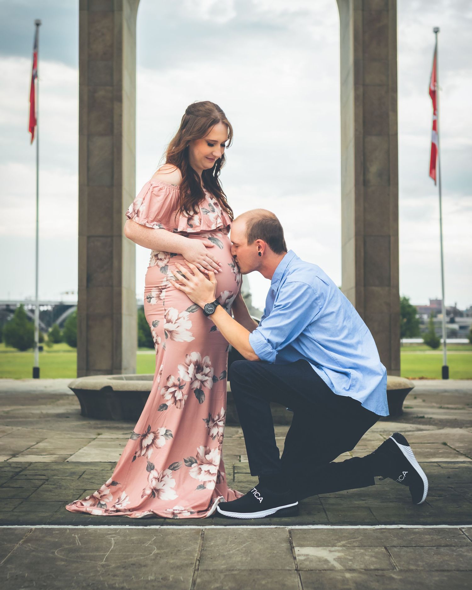 Maternity photo shoot under stone archway with flags and city backdrop in Canada.
