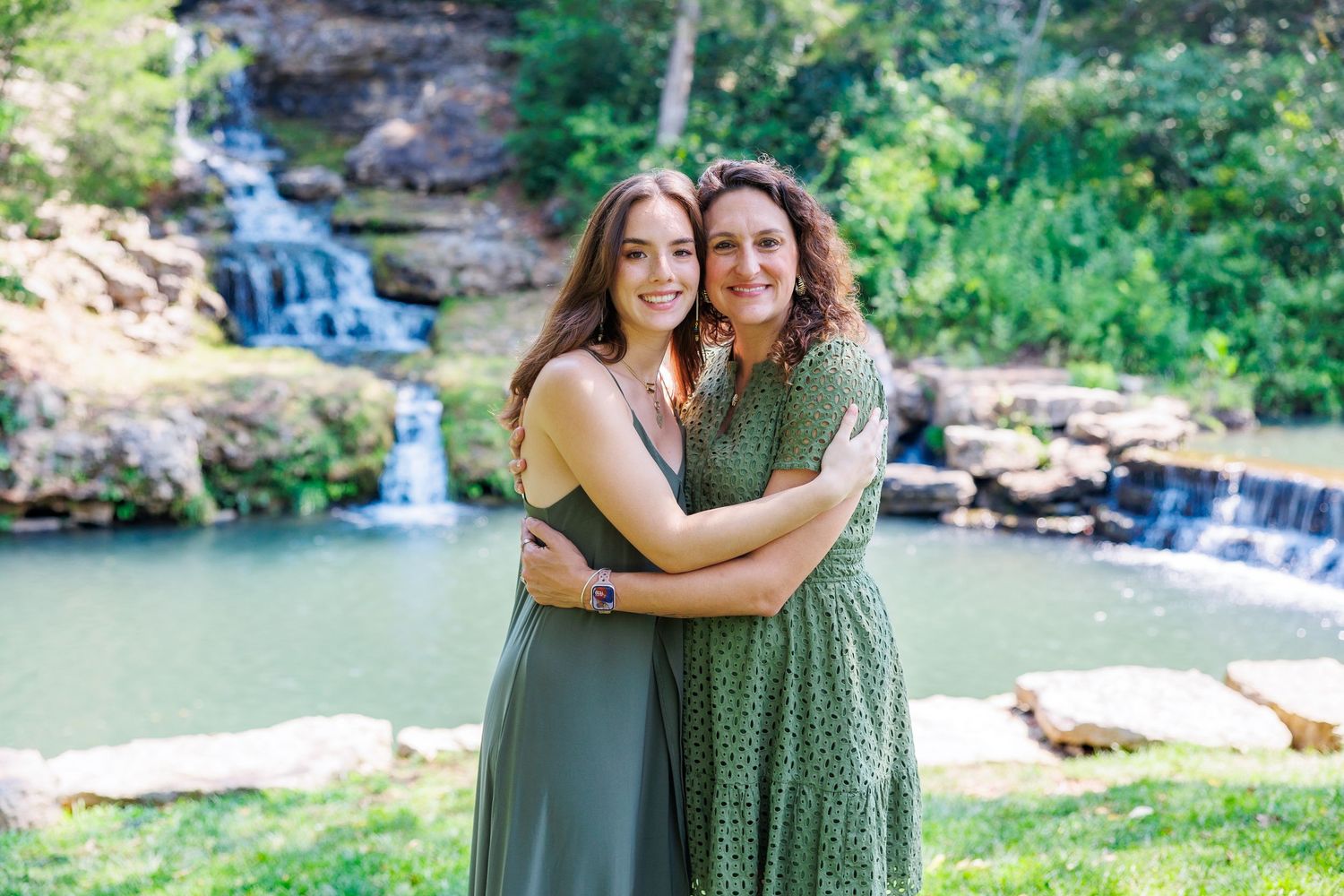 A group poses together on a viewing platform in front of a scenic waterfall cascading down rocky cliffs and by greenery at Dogwood Canyon.