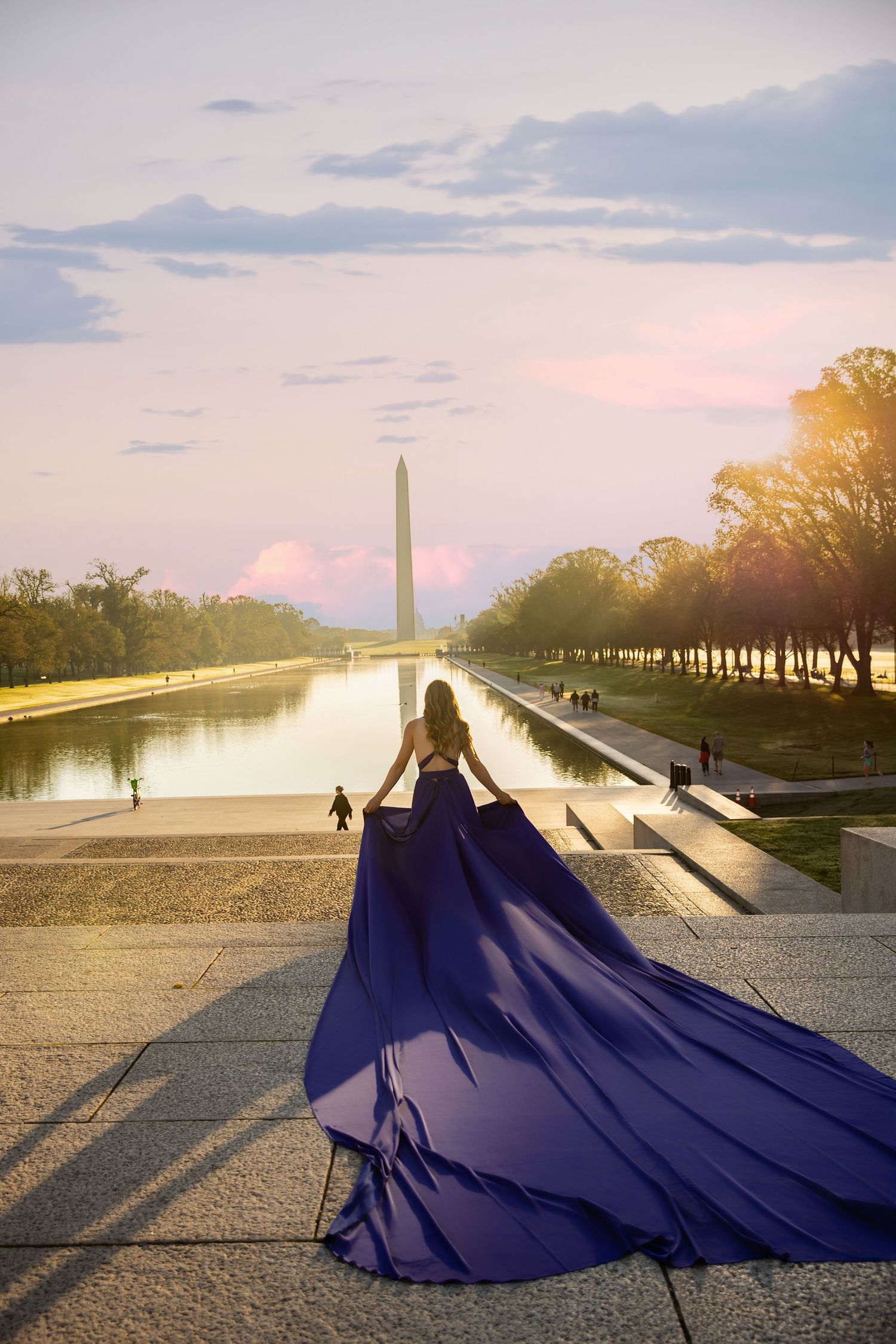 Figure in flowing navy blue gown stands before reflecting pool and Washington Monument at sunset in DC.