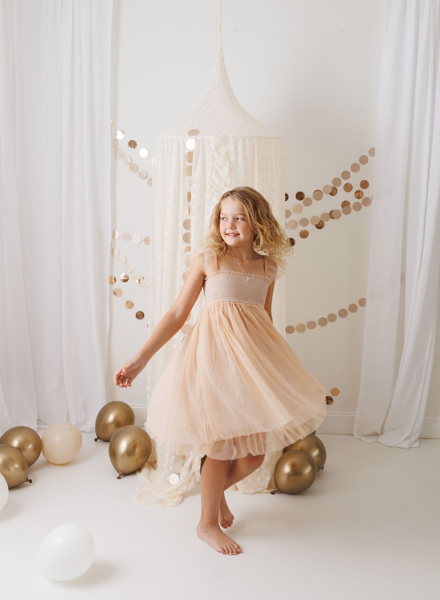 Elegant peach dress photoshoot with gold balloons and garland against white backdrop.