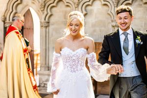 Radiant bride and groom holding hands smiling as they exit a historic stone church after their ceremony.