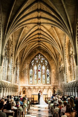 Stunning Gothic church interior with vaulted ceiling as bride and groom stand at altar before seated guests.