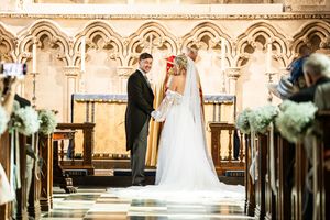 Bride and groom exchange vows at the altar of an ornate Gothic church decorated with floral arrangements.