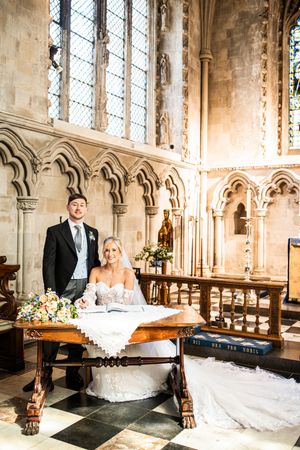 Bride and groom sign the wedding register at an ornate wooden table inside a grand historic cathedral.