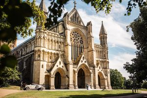 Stunning Gothic cathedral exterior on a sunny day with a vintage white car parked on the lawn.
