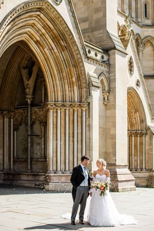 Bride and groom share a romantic moment beneath the ornate Gothic arches of a stone cathedral.