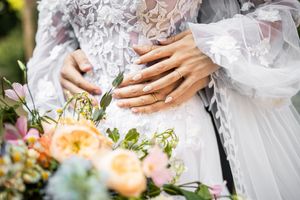 Close-up of couple embracing showing bride's lace gown details and colorful pastel wedding bouquet with peach roses.
