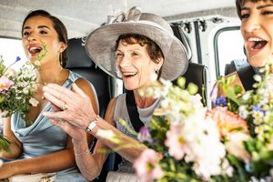 Three joyful women holding flower bouquets laughing together inside a vehicle at a wedding celebration.