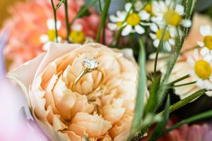 Diamond engagement ring nestled in a peach garden rose surrounded by daisies and greenery in a wedding bouquet.