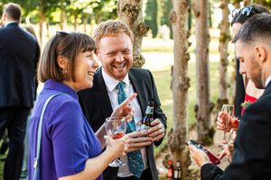 Wedding guests laughing and drinking at outdoor summer wedding reception.