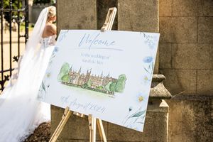 Elegant watercolor wedding welcome sign on an easel featuring an illustration of a grand English estate.