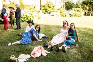 Female wedding guests relaxing on grass in colorful dresses at outdoor reception.