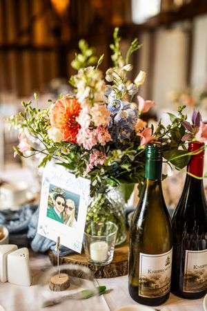Wedding table centerpiece with colorful flowers, wine bottles, and couple photo card.