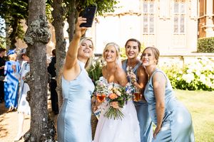 Bride and three bridesmaids in light blue dresses taking a selfie outdoors at a stately manor wedding.