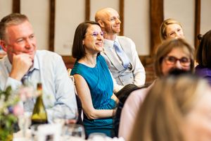 Wedding guests smile and laugh at round table during reception, woman in teal dress enjoying the celebration.