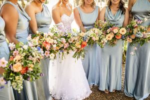 Close-up of bride and bridesmaids in blue dresses holding lush colorful floral bouquets at an outdoor wedding.