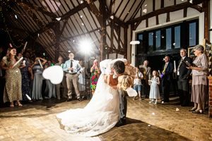 Bride and groom share first dance with guests holding white balloons in a rustic barn wedding.