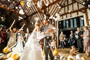 Bride and groom dance surrounded by gold and white balloons and confetti in a barn reception.