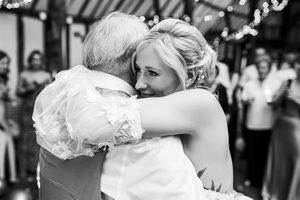Emotional black and white photo of bride sharing a tender hug during wedding reception dance.