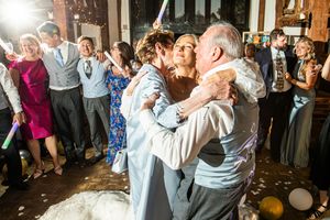 Bride and groom share a joyful group dance with family members at rustic barn wedding reception.