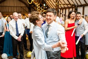 Two male wedding guests laugh and dance together joyfully at a rustic barn wedding reception.