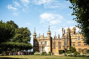 Stunning historic English manor house with ornate architecture surrounded by lush green trees on a sunny day.