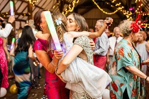 Bride shares a kiss with a guest while dancing at a lively colorful wedding reception party.