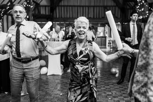 Black and white photo of elderly woman joyfully dancing with glow sticks at wedding reception.