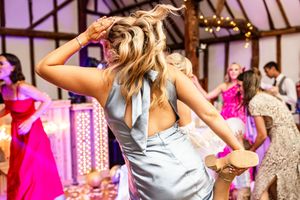 Bridesmaid in blue backless dress dancing energetically at lively wedding reception party.
