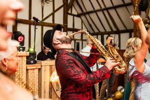 Saxophonist in red jacket performing live music at elegant wedding reception in barn venue.