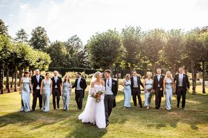 Bride and groom sharing a kiss surrounded by bridesmaids and groomsmen on a sunny lawn at a manor wedding.