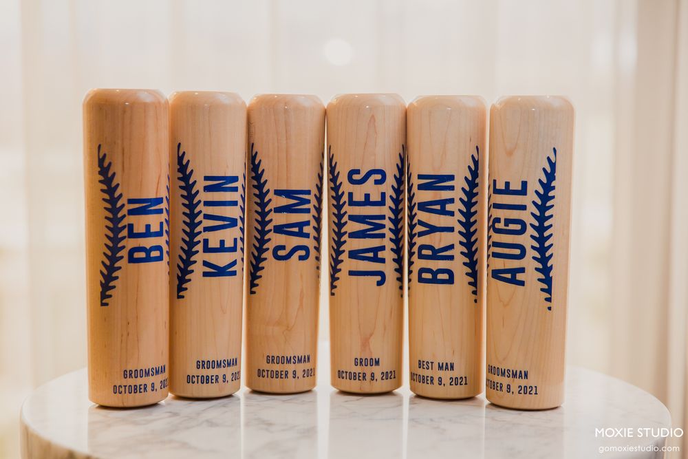 Six wooden groomsmen gift flasks with names and wheat designs arranged in a row.