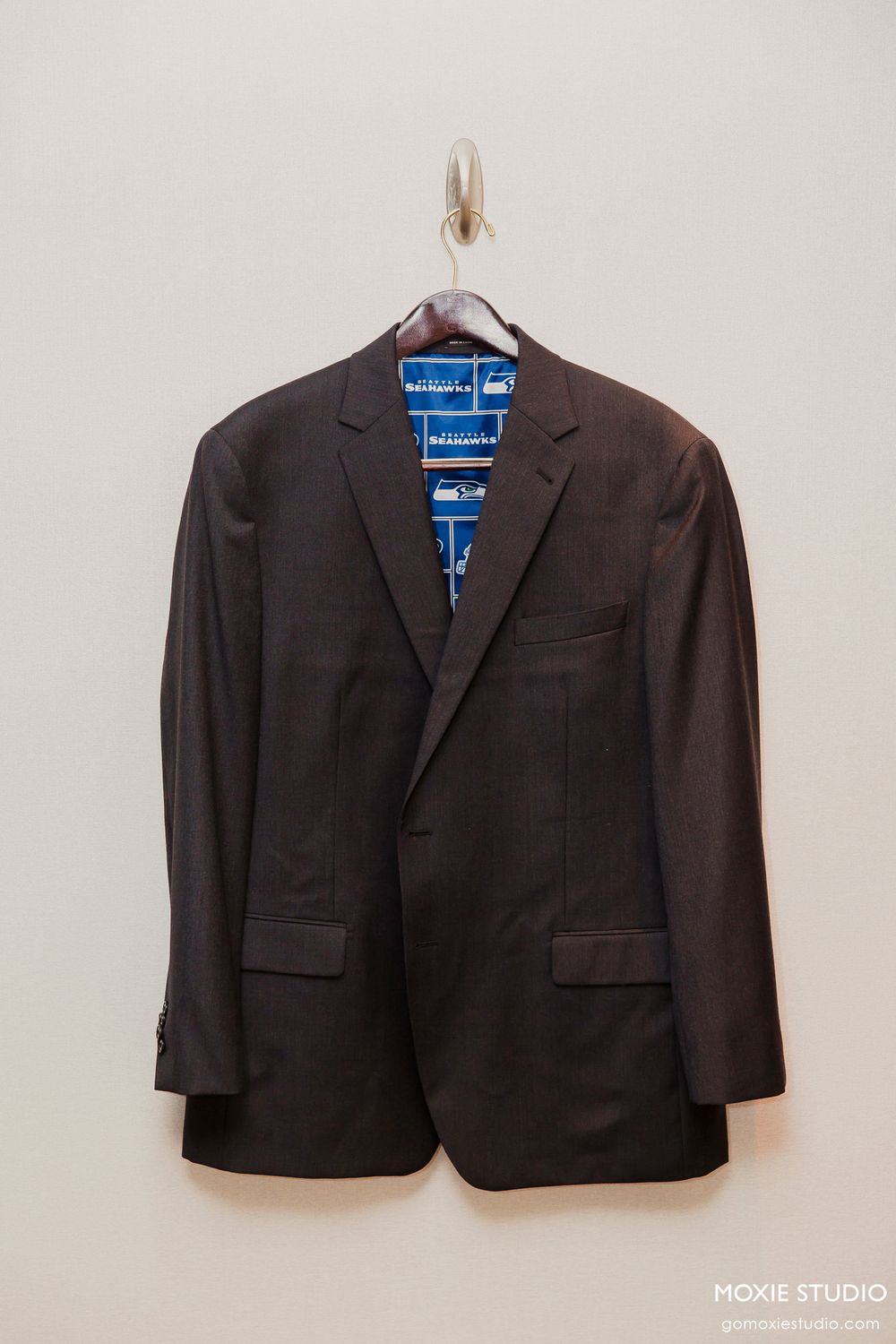 Black formal suit jacket hanging on display against a white wall.