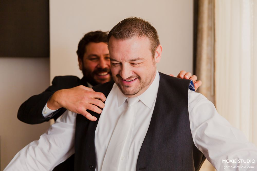 Two people in formal attire share a candid laughing moment together during what appears to be a wedding event.