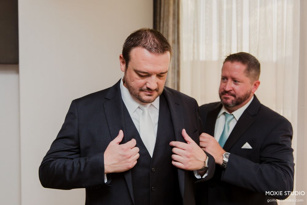 Two men in formal suits share a candid moment during wedding preparations.