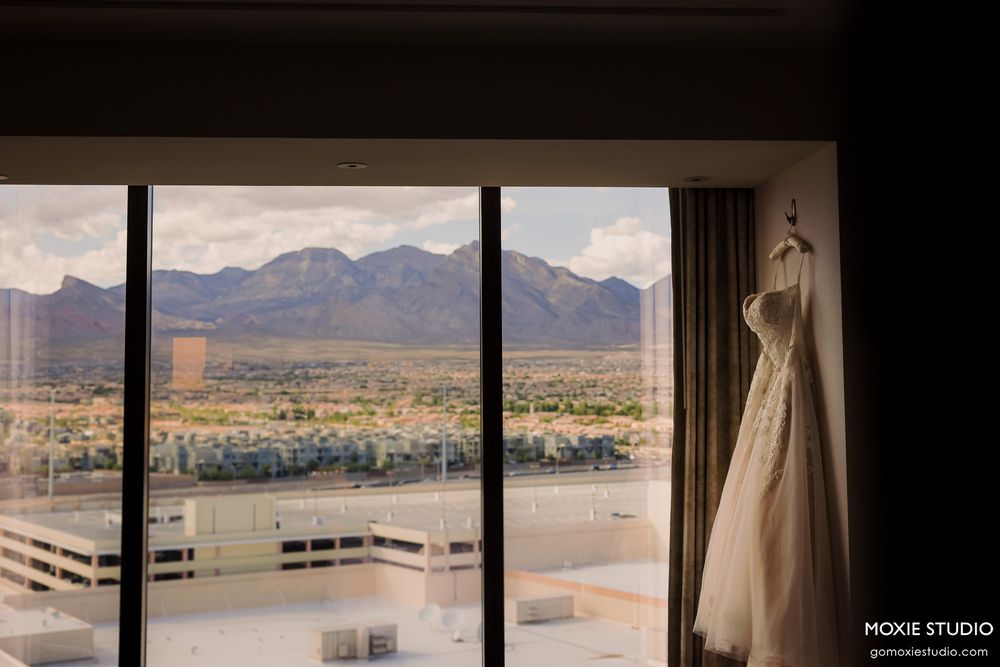 White wedding dress hangs by window overlooking mountain landscape and desert valley.