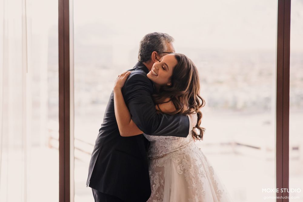 A couple shares an intimate embrace in front of large windows during their wedding day.